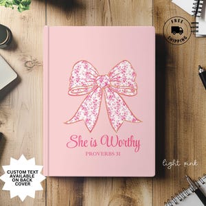 May include: Light pink journal with a gold bow with a floral pattern and the text "She is Worthy Proverbs 31".