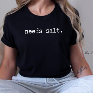 May include: A black t-shirt with the text "needs salt." printed in white.