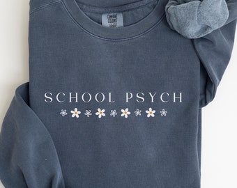 May include: A blue sweatshirt with the text "SCHOOL PSYCH" in white lettering and a row of white daisies with yellow centers.