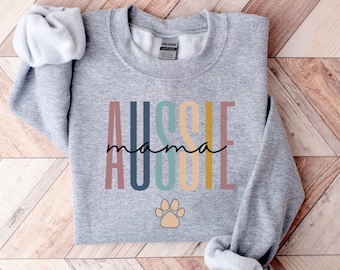 Puede incluir: Sudadera gris con el texto "Aussie mama" en colores arcoíris y una huella de pata.