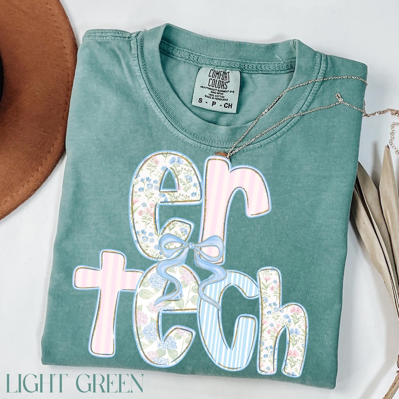 May include: Light green t-shirt with the word "ER TECH" in a floral and striped design. The letters are decorated with a floral pattern, pink stripes, and blue stripes. A light blue bow is between the letters "ER". The shirt has a Comfort Colors tag.