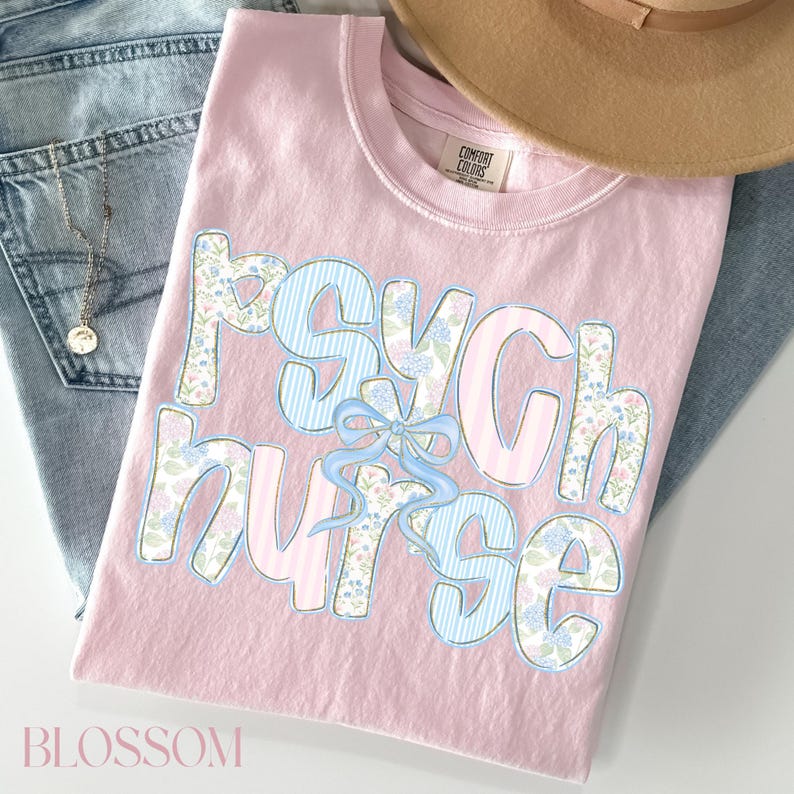 May include: A pale pink Comfort Colors t-shirt featuring the words "Psych Nurse" in a floral and striped design. A light blue bow is between the words. The shirt is on blue jeans and a tan hat.