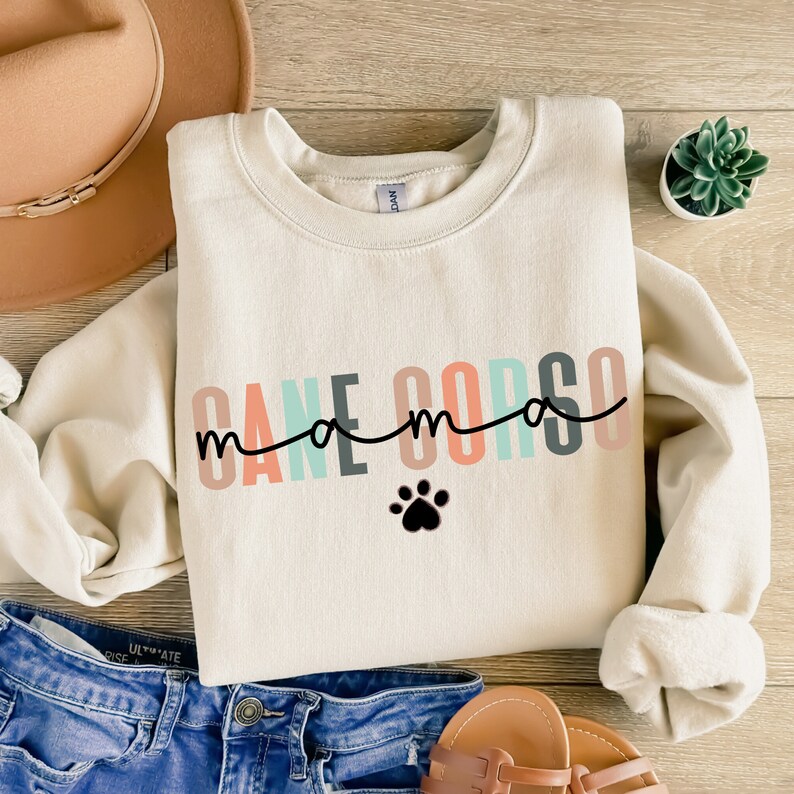 May include: A cream-colored sweatshirt with the text "Cane Corso mama" in rainbow colors and a black paw print.