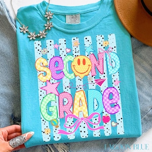 Peut inclure: Un t-shirt turquoise Comfort Colors avec un graphisme coloré "Second Grade". Le motif comprend un smiley, des étoiles, des nœuds et un motif à carreaux. Le t-shirt est décoré de rayures verticales et de petits pois.