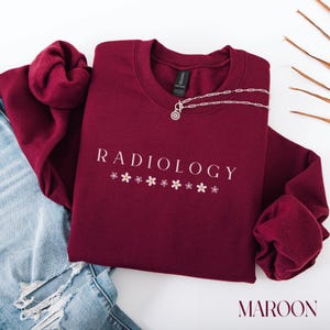 May include: Maroon sweatshirt with the text "RADIOLOGY" in white with small pink flowers underneath.