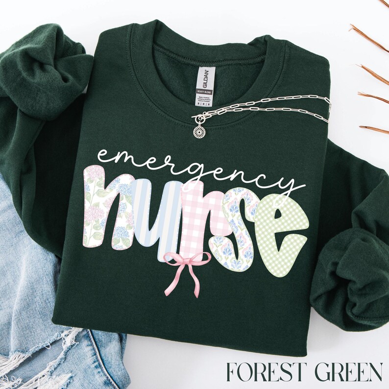 Puede incluir: Sudadera verde bosque con las palabras "emergency nurse" en una fuente caprichosa. Las letras est&aacute;n decoradas con estampados florales, de cuadros y de rayas. Un collar plateado con un colgante est&aacute; sobre la sudadera. Las palabras "FOREST GREEN" est&aacute;n abajo.
