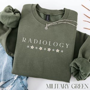 May include: A green sweatshirt with the text "RADIOLOGY" in white lettering and a row of small white flowers underneath. The sweatshirt is on a blue denim background.