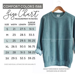 May include: Blue spruce adult crewneck sweatshirt on a wooden hanger. The image includes a size chart with measurements in inches for width, length, and sleeve length. The chart shows sizes S to 3X.