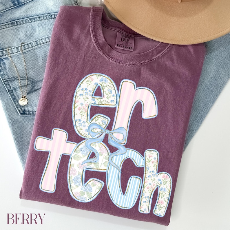 May include: A berry-colored t-shirt with the words "er tech" in a floral and striped design. The shirt is folded on top of a pair of blue jeans and a tan hat. The word "BERRY" is printed at the bottom left.