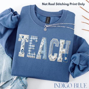 May include: Indigo blue sweatshirt featuring the word "TEACH" in a patchwork design with floral and gingham patterns. A silver chain necklace with a pendant is on the sweatshirt. The text "Not Real Stitching Print Only" is at the top.