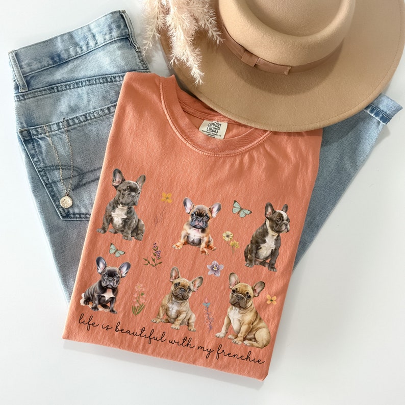May include: A peach-coloured t-shirt with a graphic of five French Bulldogs and the text "life is beautiful with my frenchie".