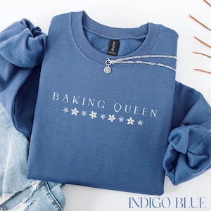 May include: Indigo blue sweatshirt with the text "Baking Queen" and a row of white daisy flowers.