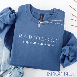 May include: Indigo blue sweatshirt with the text "RADIOLOGY" in white lettering and a row of white daisy flowers below the text.