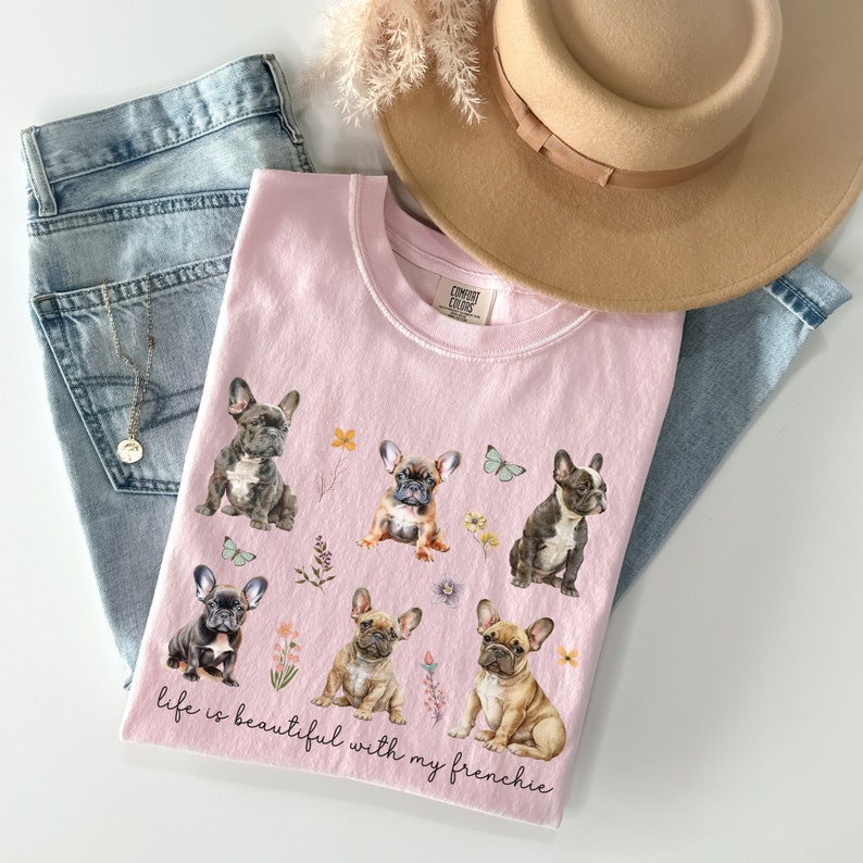 May include: Pink t-shirt featuring a graphic of six French Bulldogs and the text "Life is beautiful with my frenchie".