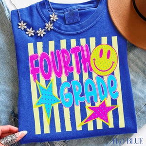Op de afbeelding: Blauw T-shirt met de tekst "FOURTH GRADE" in roze en turquoise, een gele smiley en twee sterren. Het shirt heeft gele verticale strepen en is van het merk Comfort Colors.