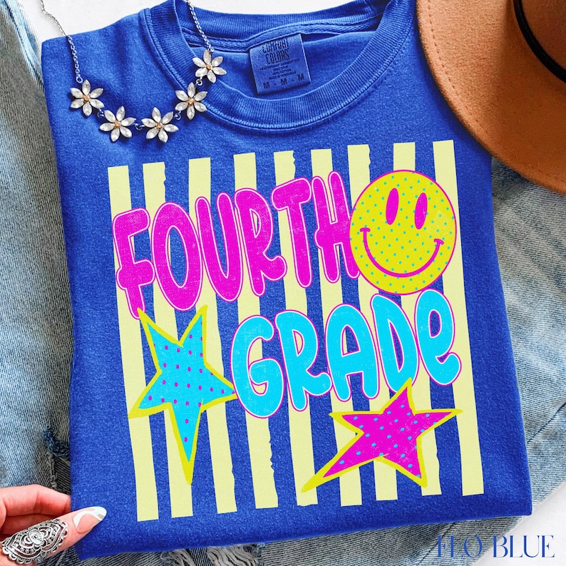 Op de afbeelding: Blauw T-shirt met de tekst "FOURTH GRADE" in roze en turquoise, een gele smiley en twee sterren. Het shirt heeft gele verticale strepen en is van het merk Comfort Colors.