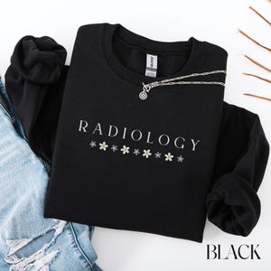 May include: Black sweatshirt with the text "RADIOLOGY" in white lettering and a row of small white flowers below the text.
