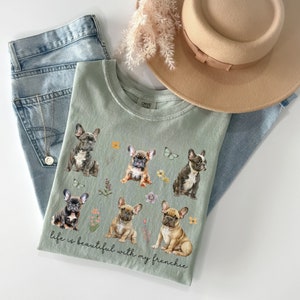 May include: Sage green t-shirt featuring a graphic of six French Bulldogs and flowers. The text "life is beautiful with my frenchie" is printed on the shirt.