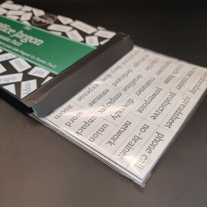 May include: A set of white cards with black text, featuring common office jargon terms. The cards are arranged in a stack, with the top card showing the text "phone call". The cards are labeled with terms like "spreadsheet", "water cooler", "touch base", "powerpoint", "network", "computer", "customer", "diversify", "union", "corporate", "deep dive", "expense", "manage", "dedicated", "estimate", "capable", "deadline", "employer", "unpack", "word", "zoom", "sale", "pin", "shred", "copy", and "graph".