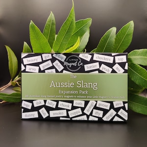 May include: A box of magnetic poetry words with an Australian slang theme. The box is green and white with the words "The Aussie Slang Expansion Pack" printed on it. The words on the magnets include "arvo", "chook", "drongo", "smoko", "togs", and "dunny".