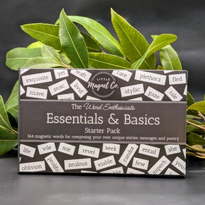 May include: A black box with the words "Essentials & Basics" and "The Word Enthusiasts" printed on it. The box contains 564 magnetic words for composing stories, messages, and poetry. The words are printed on small, black rectangular tiles.
