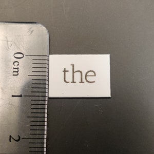 May include: White tile with the word "the" printed in brown lettering.