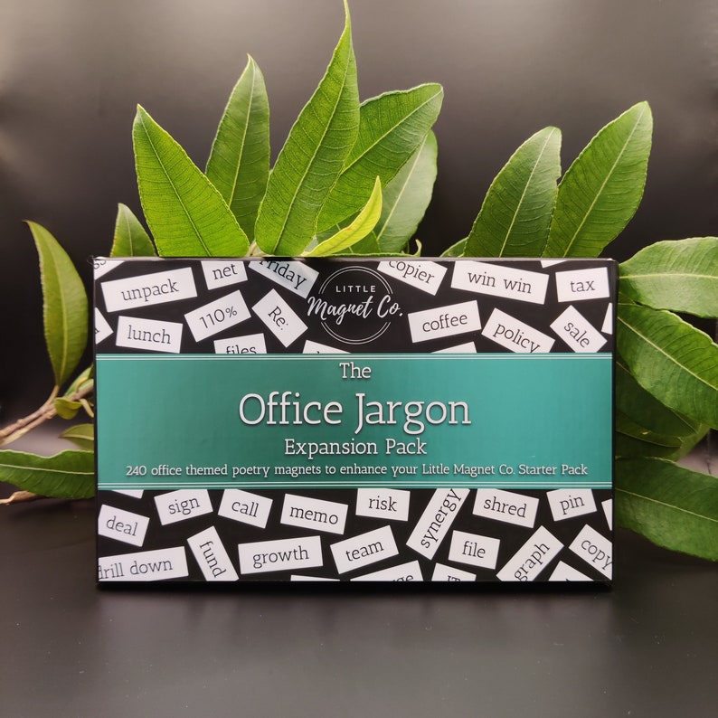 May include: A black box with a teal border and white text that reads "The Office Jargon Expansion Pack". The box contains 240 office themed poetry magnets to enhance your Little Magnet Co. Starter Pack. The box is surrounded by green leaves.