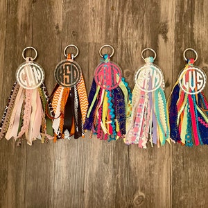 May include: Five colorful keychains with different initials on each. The keychains are made of clear acrylic with a white circle around the initials. The keychains are attached to a silver ring and have a variety of colorful ribbons attached to the ring.