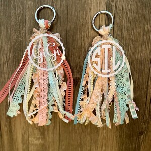 May include: Two keychains with a circle of clear acrylic with a monogram on each. The keychains are made with a variety of colorful ribbons and lace.