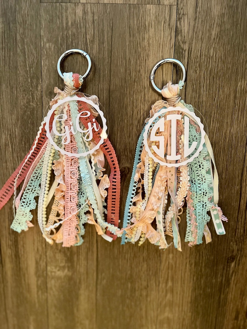 May include: Two keychains with a circle of clear acrylic with a monogram on each. The keychains are made with a variety of colorful ribbons and lace.