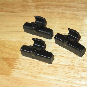 May include: Three black plastic bike brake blocks with a metal clip on each.