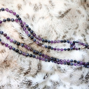Könnte beinhalten: Eine zweireihige Halskette aus Amethyst- und Saphirperlen. Die Halskette liegt auf einer weißen Kunstfell-Oberfläche.