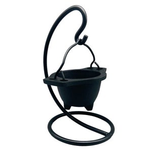May include: A black metal cauldron with a curved handle and a circular base. The cauldron has a small bowl shape and is suspended from a curved metal stand. The stand has a circular base and a hook at the top.