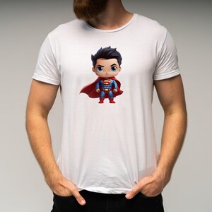 May include: White t-shirt featuring a cartoon image of Superman in a red cape and blue suit. The Superman character is in a chibi style, with a large head and small body.