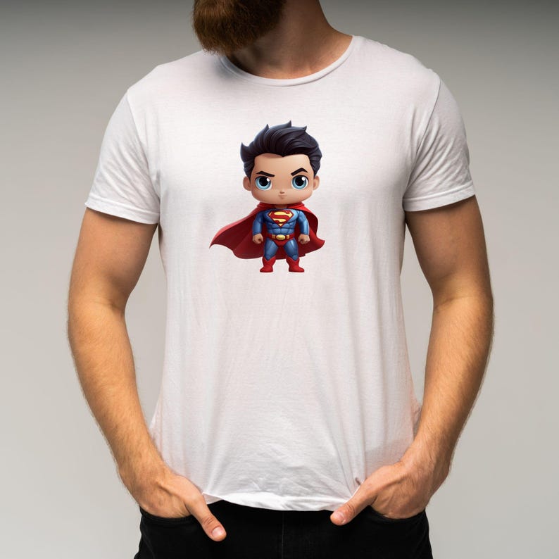 May include: White t-shirt featuring a cartoon image of Superman in a red cape and blue suit. The Superman character is in a chibi style, with a large head and small body.