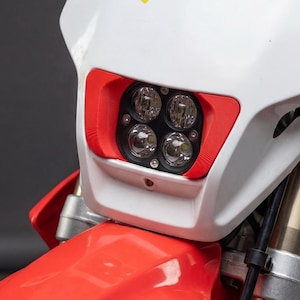 May include: White and red motorcycle headlight assembly with four LED lights. The headlight has a red trim and a yellow and black Acerbis logo. The motorcycle's front fender is red.