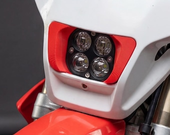 May include: White and red motorcycle headlight assembly with four LED lights. The headlight has a red trim and a yellow and black Acerbis logo. The motorcycle's front fender is red.