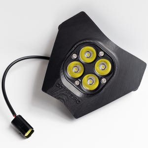 Puede incluir: Conjunto de luces LED negras con cuatro luces amarillas brillantes. El conjunto tiene una superficie texturizada y un cable negro con un conector. La palabra "DO ENDURO" está impresa en el lateral.