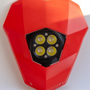 Könnte beinhalten: Ein roter Motorradscheinwerfer mit vier hellen LED-Leuchten. Der Scheinwerfer hat einen schwarzen Rahmen um die Lichter und der Text "DO ENDURO" ist sichtbar. Das Gehäuse ist leuchtend rot.