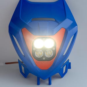 May include: A blue and orange motorcycle headlight assembly with two bright LED lights. The headlight has a distinctive angular design and the text "OOENDURO" is visible on the orange section.