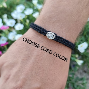 May include: A black braided bracelet with a silver oval charm. The bracelet is on a person's wrist. CHOOSE CORD COLOR.
