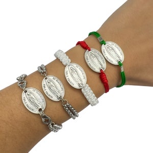 Könnte beinhalten: Vier Armbänder mit silbernen Anhängern, die das Bild der Jungfrau von Guadalupe zeigen. Die Armbänder sind aus weißem, rotem und grünem Garn gefertigt.