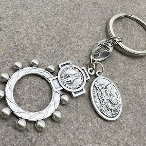 May include: Silver keyring with a circular rosary ring, a cross charm with the words "Regina Sine Labe Original" and a Saint Michael charm with the words "St. Michael" and "Italy".