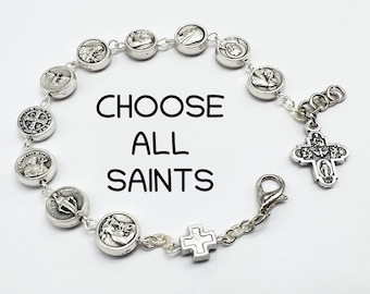 May include: Silver bracelet with a silver cross charm and multiple round charms featuring images of saints. The bracelet has a lobster clasp closure. The text "CHOOSE ALL SAINTS" is printed on a white background.