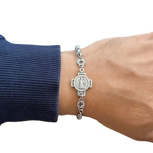 May include: A silver chain bracelet with a silver charm featuring a cross and a depiction of the Virgin Mary.