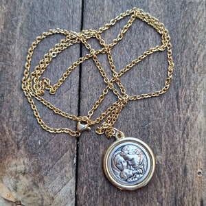 May include: A gold chain necklace with a silver pendant featuring a detailed image of a family. The pendant is round and has a raised design.