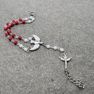 May include: A white and red beaded rosary with a silver dove and cross pendant.