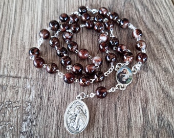 May include: Brown and white rosary beads with a silver chain and a silver pendant featuring a picture of Saint Anthony. The pendant has the text "St. Anthony 1904" on it.