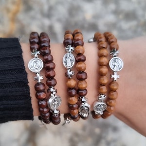 Può includere: Quattro braccialetti di perline di legno marrone con ciondoli d'argento raffiguranti figure religiose e croci.