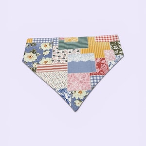 May include: A patchwork bandana featuring a variety of fabric patterns, including floral, gingham, and striped designs. The bandana is a mix of colors, including blue, red, yellow, and pink. The bandana is a triangle shape.